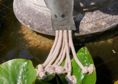 Olive the Octopus eco-friendly dog toy made from jute and suede resting beside a garden water feature.