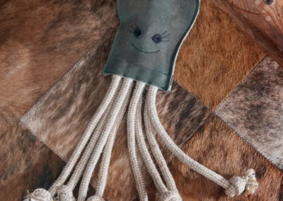 Olive the Octopus eco dog toy with rope legs lying on a patterned rug indoors.