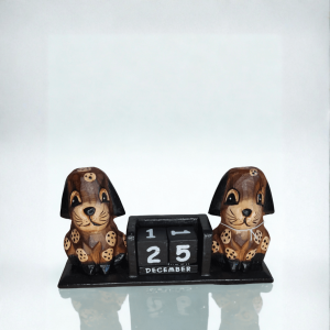 Hand-carved wooden dog perpetual calendar featuring two brown spotted dogs on either side of black date blocks displaying “25 December.” A charming handmade wooden desk ornament.
