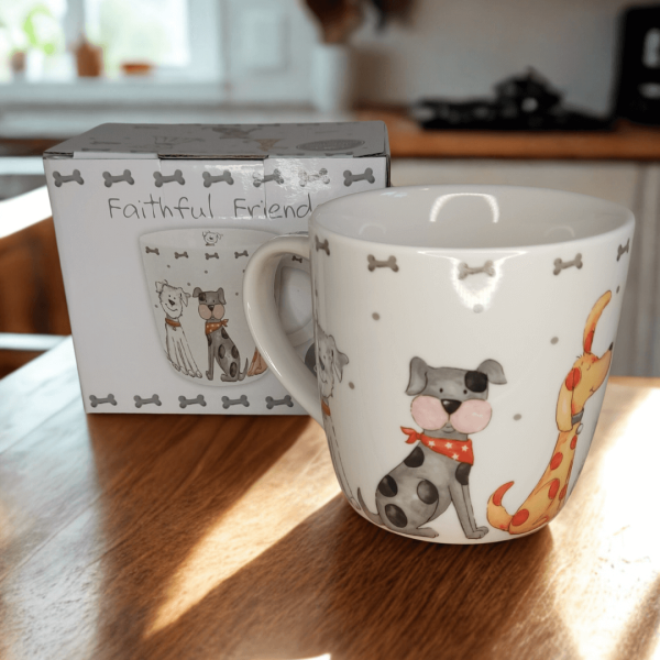 Faithful Friends fine china dog mug displayed beside its matching gift box on a wooden table. The design features cheerful illustrated dogs with grey bone accents on a white background.