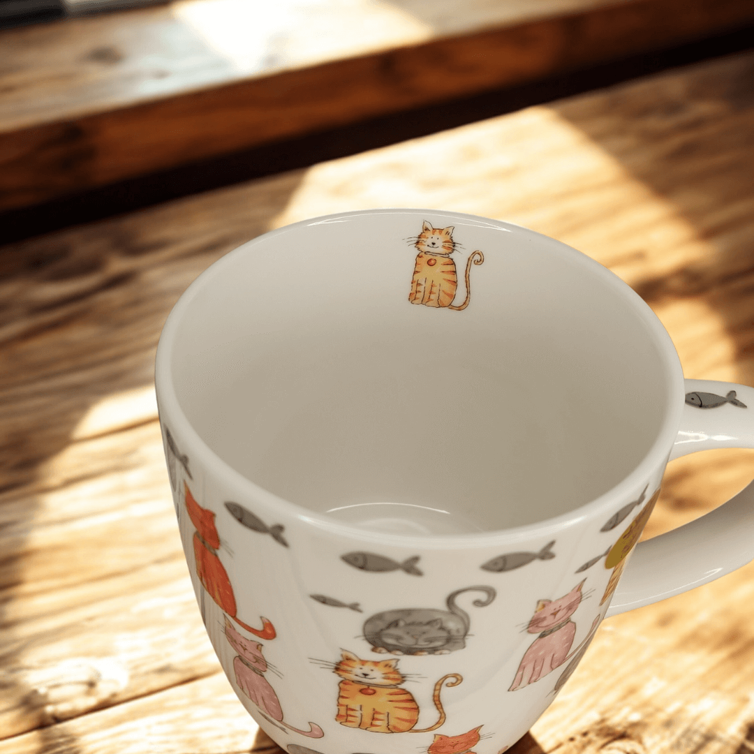 Close-up of the Faithful Friends cat mug showing the interior design with a small orange tabby cat illustration on the inner rim. The mug is decorated with playful cat and fish patterns on a white background.