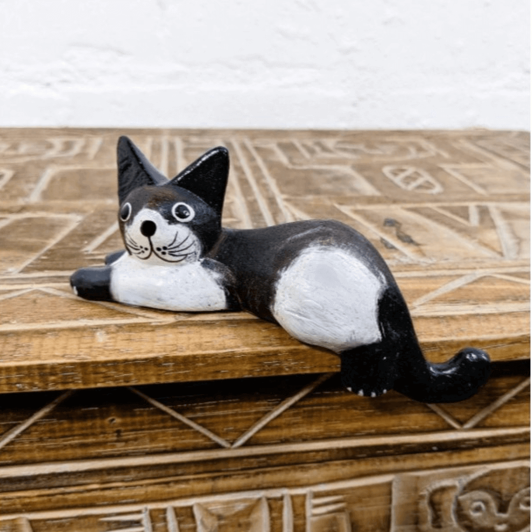 Black and white hand-carved wooden cat shelf sitter displayed on a patterned wooden table. A charming handcrafted ornament made in Bali.