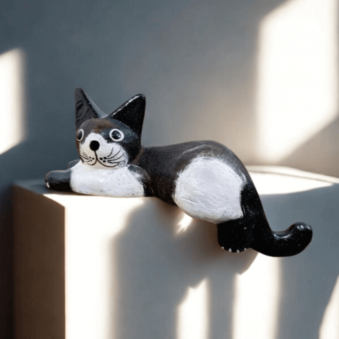 Hand carved black and white wooden shelf sitter cat ornament resting on a ledge in soft natural light. A playful handmade décor piece for cat lovers.