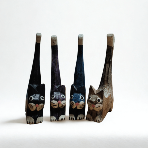 Group of four hand-carved wooden cat ornaments in assorted colours — black, purple, blue, and natural wood — shown against a plain white background. Each cat has a tall tail and painted facial details, highlighting their handmade charm.