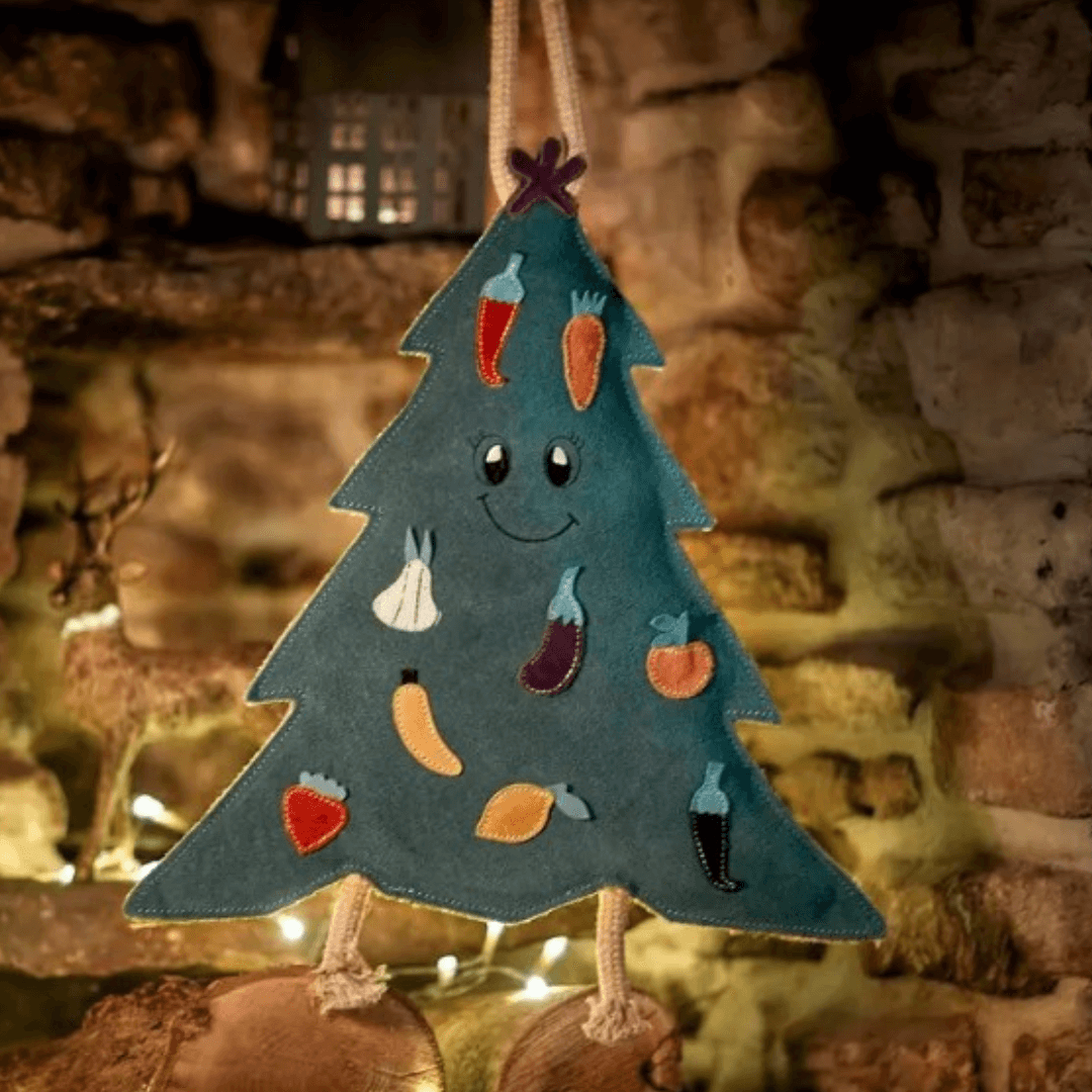 Carol the Christmas Tree eco dog toy displayed by a fireplace with festive lights – natural jute and suede Christmas dog toy.
