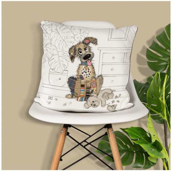 Murphy Mutt dog design cushion from the Bug Art Collection displayed on a white chair with green houseplants in the background. The cushion shows a cheerful patchwork-style dog sitting beside a chewed toy, adding a fun and homely touch to the décor.