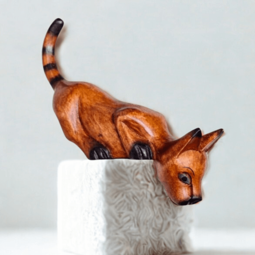 A wooden shelf sitter cat ornament looking down over a ledge on a white background