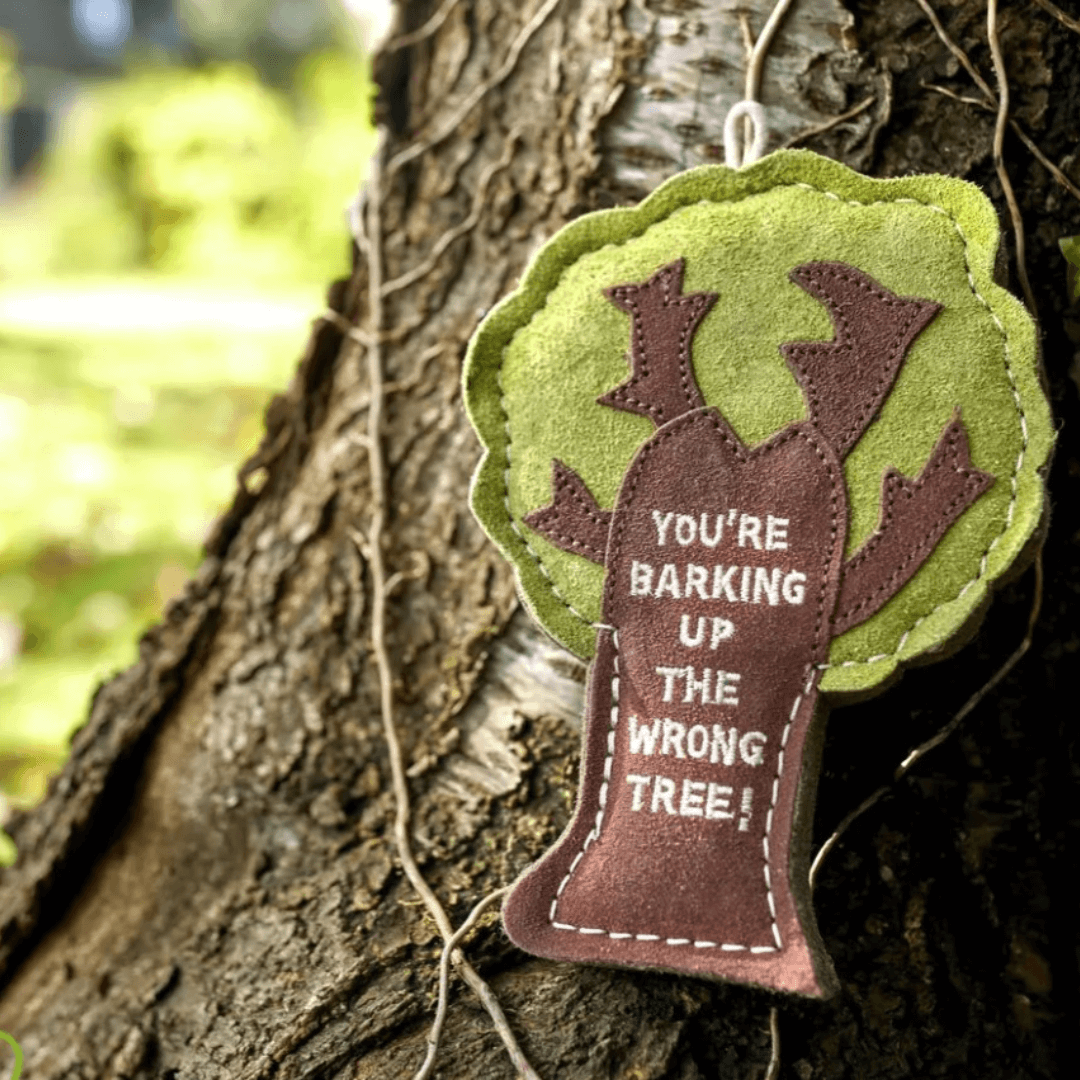 Eco-friendly felt and suede dog toy shaped like a tree hanging outdoors on real bark, with the phrase “You’re Barking Up the Wrong Tree” embroidered on the front.