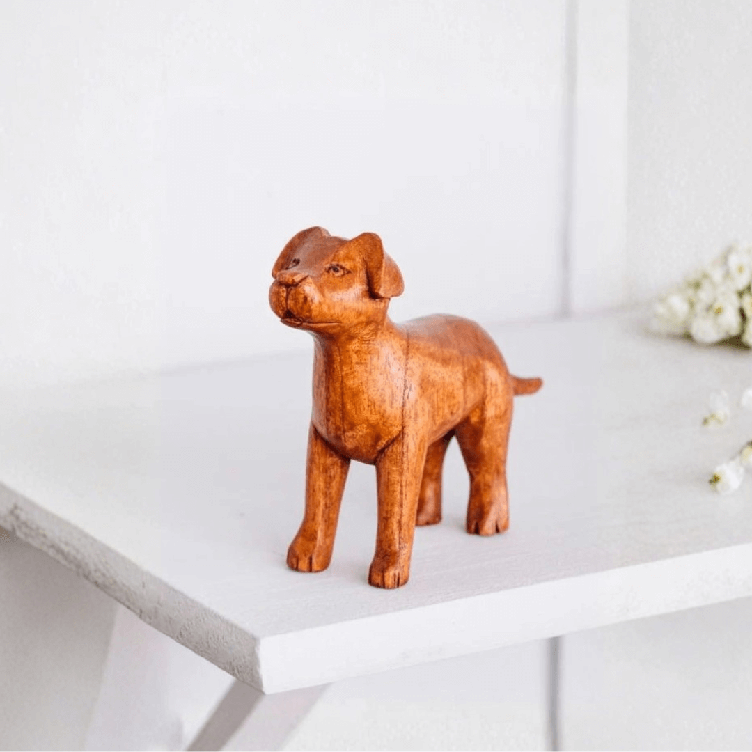 Hand-carved brown wooden standing dog ornament displayed on a white shelf.